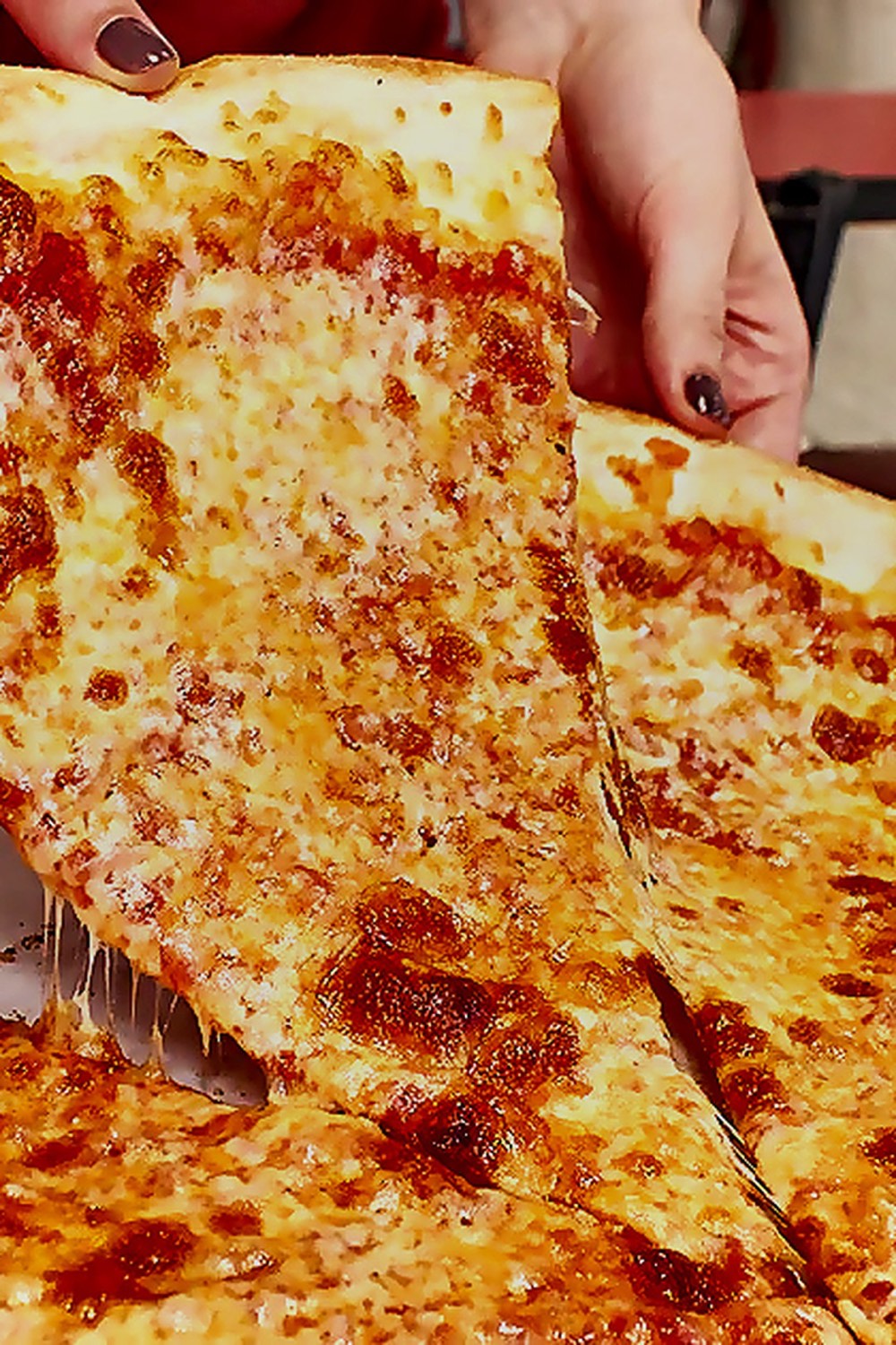 Hand lifting a New York style cheese slice from a whole pie at Gigi's